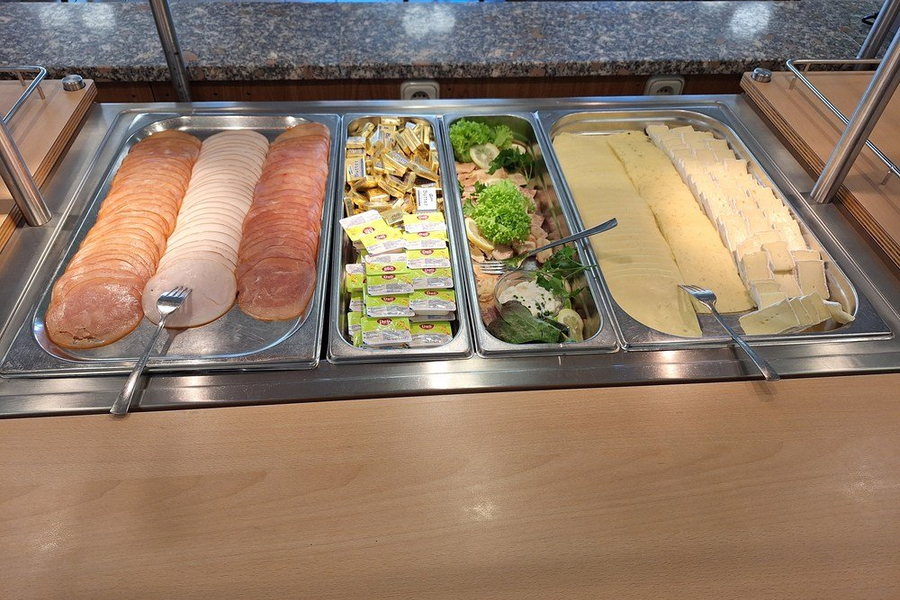 Buffet mit Aufschnitt: Scheiben von Wurst und Käse, Butterportionen und Salat mit Gurken und Tomaten.