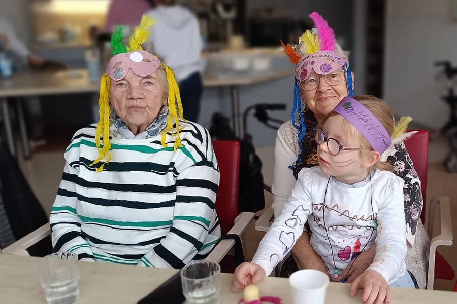 Zwei Kinder mit bunten Federkopfbändern sitzen an einem Tisch mit Bastelmaterialien und Getränkegläsern.