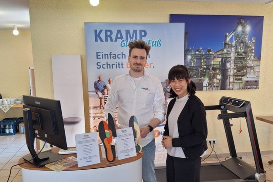 Zwei Personen stehen an einem Messestand mit dem Schriftzug 'KRAMP Gut zu Fuß', im Hintergrund ein Laufband und ein Plakat mit Fußabdruck und Text.