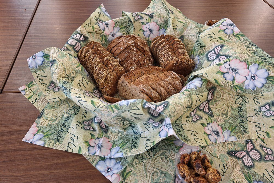 Mehrere Scheiben Vollkornbrot und ein ganzes Brot liegen auf einem grünen, mit Blumen und Schmetterlingen bedruckten Tuch auf einem Holztisch.