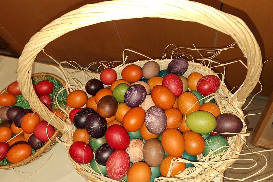 Geflochtener Korb mit vielen bunten Ostereiern in verschiedenen Farben und Mustern, darunter rot, orange, grün, lila und braun.