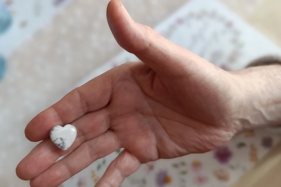 Offene Hand mit einem kleinen, herzförmigen Stein mit grauen Adern auf der Handfläche.