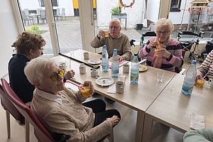 Mehrere ältere Menschen sitzen an einem Tisch und trinken aus Gläsern mit Strohhalmen.