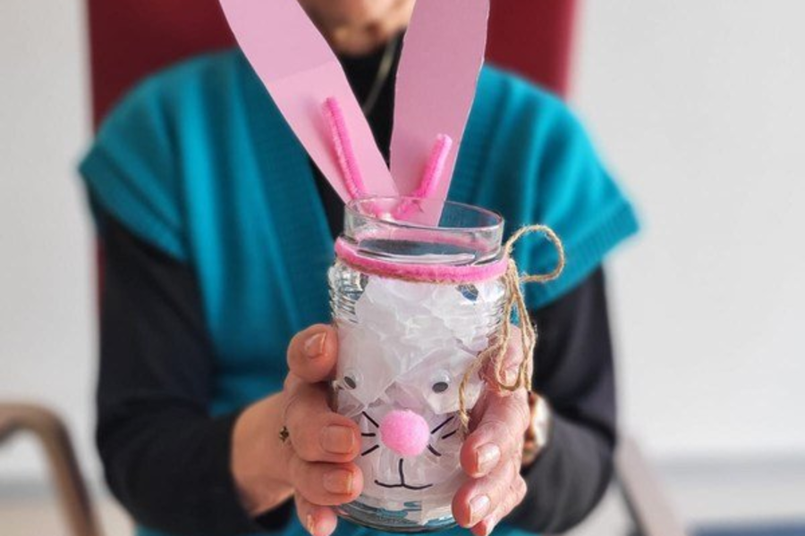 Person hält ein Glas mit einer Hasen-Dekoration aus rosa Papierohren, rosa Nase und Schnurrhaaren aus Draht.