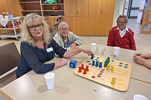 Aktive Senioren bei einem Spielabend mit bunten Spielefiguren, Würfeln und Getränken am Tisch