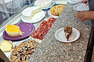 Theke mit verschiedenen Kuchenstücken und einer Person, die einen Teller hält