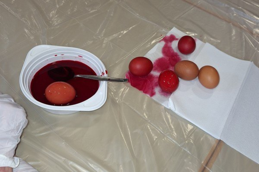 Mehrere Eier liegen auf einem weißen Papier, daneben ein Behälter mit roter Flüssigkeit und einem Löffel, alles auf einer durchsichtigen Plastikfolie.