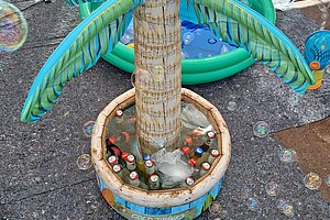 Aufblasbare Palme mit Flaschen im Wasserbecken und Seifenblasen auf gepflastertem Boden