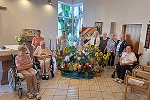 Altar mit Marienstatue, umgeben von Sonnenblumen, weiteren Blumensträußen, Kerzen und religiösen Bildern in einem Raum mit Fliesenboden