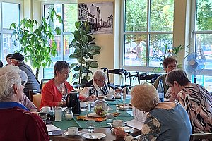 Mehrere ältere Menschen sitzen an einem Tisch in einem hellen Raum und essen gemeinsam