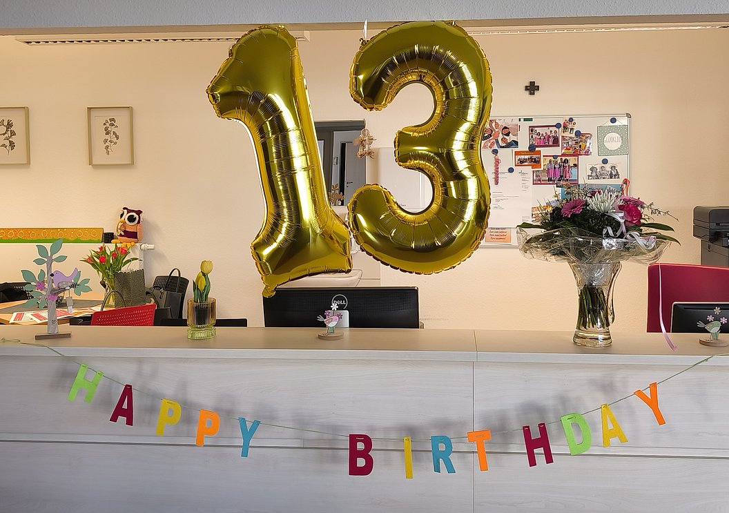 Goldene 13 und bunte "HAPPY BIRTHDAY"-Girlande an Empfangstresen, mit Blumen und Deko.
