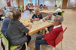 Mehrere ältere Menschen sitzen an Tischen in einem Gemeinschaftsraum und spielen Gesellschaftsspiele