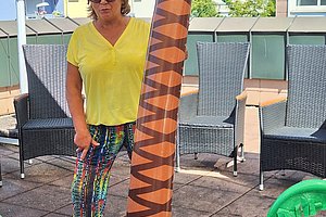 Person steht neben aufblasbarer Palme in kleinem Planschbecken mit mehreren gelben Gummienten auf Terrasse mit Gartenmöbeln