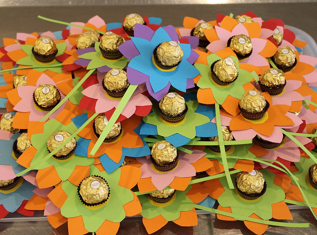 Bunte Papierblumen mit goldverpackten Pralinen in der Mitte, auf einem Tisch angeordnet.
