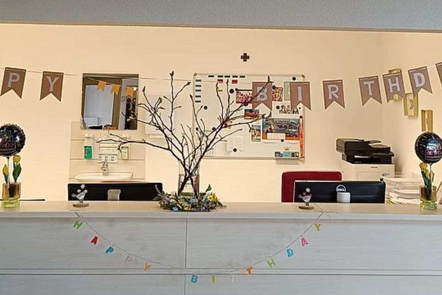 Weiße Theke mit Dekorationen, darunter goldene Luftballons in Form der Zahl 21, Girlanden mit Buchstaben und Zweig in Vase.