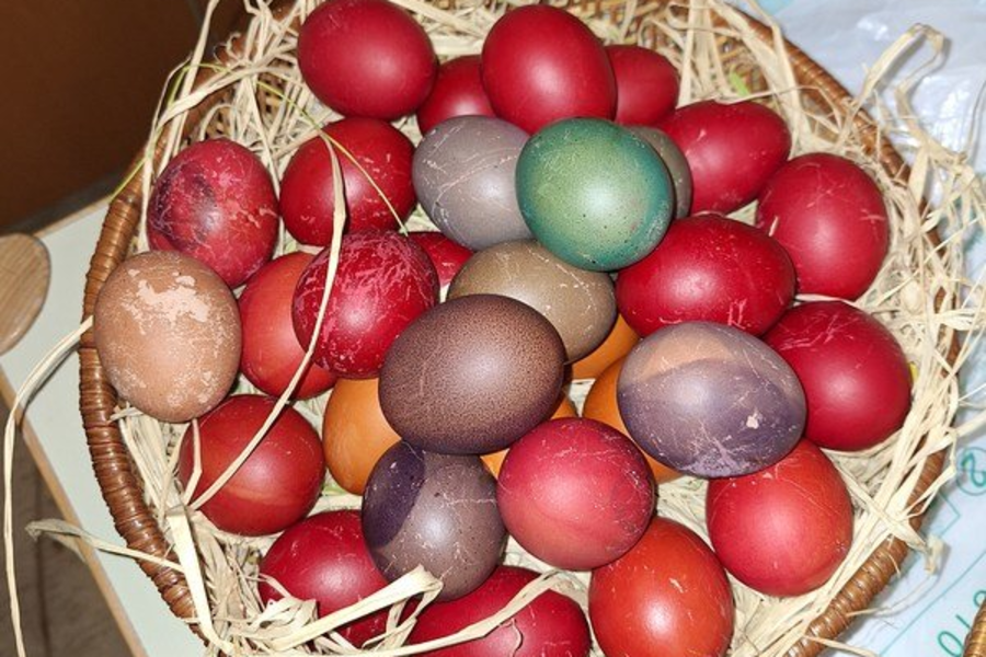 Korb mit gefärbten Eiern in verschiedenen Rottönen, einigen braunen und einem grünen Ei, auf Stroh gebettet.