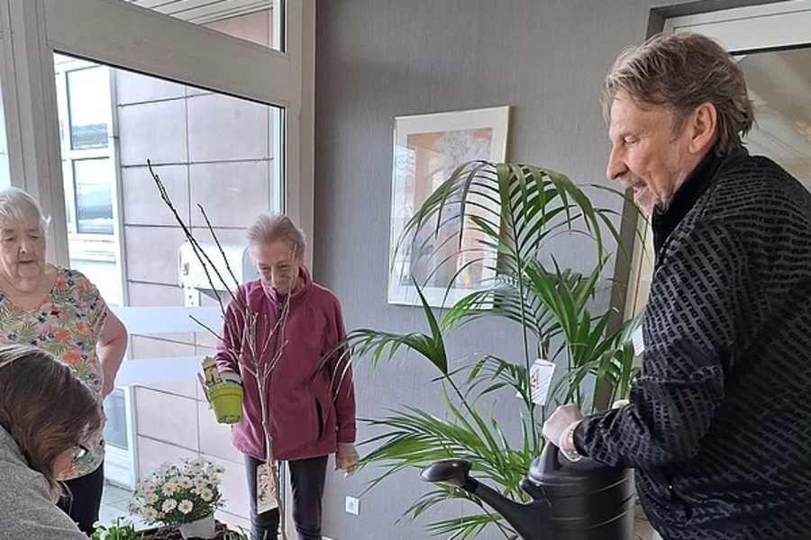 Mehrere Personen pflanzen bunte Blumen in ein großes, rechteckiges Hochbeet in einem Innenraum.