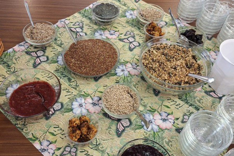 Tisch mit grünem, floral gemustertem Tuch, darauf mehrere Schalen mit verschiedenen Körnern, Samen, Trockenfrüchten und Gläser mit Wasser.
