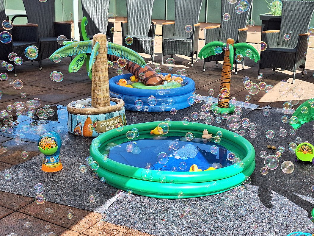 Mehrere aufblasbare Planschbecken und Palmen mit Spielzeugenten und Seifenblasen auf einer Terrasse